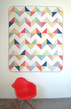 a red chair sitting in front of a wall quilt