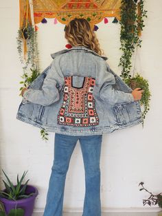 a woman standing in front of a white wall wearing a jean jacket with an embroidered design on the back