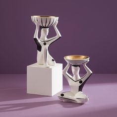 two white vases sitting next to each other on a purple surface