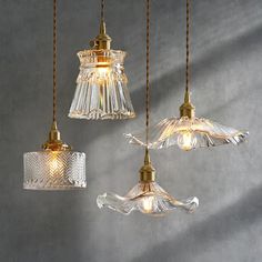 three glass pendant lights hanging from rope against a gray wall, one light is gold and the other is clear