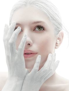 a woman with white gloves on her face and hands near her face, looking at the camera