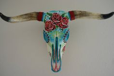 a bull's skull with long horns decorated with flowers and roses on it is hanging from the wall