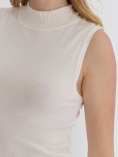 Add a touch of quirkiness to your wardrobe with the LYDIA HIGH NECK SLEEVELESS TOP. Featuring button detail at the shoulder and available in three fun colors, this knit top is perfect for those who don't take themselves too seriously. Style with your favorite jeans for a unique and fun outfit. 100% Nylon See size chart in photos. Casual White Seamless Knit Top, Stretch Knit High Neck Tops, Stretch Knit High-neck Tops, Ribbed Neckline Knit Turtleneck Tops, Knit Turtleneck Top With Ribbed Neckline, Seamless Sleeveless Top For Fall, White High Neck Cotton Top, Trendy High Neck Knit Top For Spring, Trendy Turtleneck Tank Top For Summer