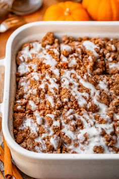 a white casserole dish filled with cinnamon rolls and topped with icing next to oranges