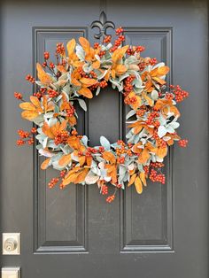 a wreath with orange and green leaves is hanging on the front door's black door