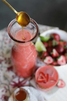 a spoon pouring liquid into a jar filled with strawberries and cucumber slices