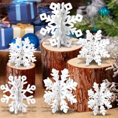 three snowflakes sitting on top of wooden logs next to christmas tree stumps