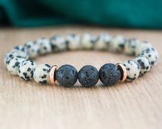 "Our Lava Stone and Dalmatian Jasper Bracelet is a beautiful accessory that offers more than just style. Made with 8 mm lava stones in the center, and Dalmatian Jasper beads, complemented by gold-colored stainless steel spacer discs, this bracelet is designed to help you stay grounded and balanced throughout your day. The beads are strung on a durable stretch cord, allowing for easy on/off fit. The finishing knot is not visible on this item. Whether you're looking for a unique piece of jewelry to add to your collection or a meaningful gift for someone special, this bracelet is sure to impress. Designed to be a perfect gift for her whether you're by her side or miles apart. Your jewelry will arrive in organza bag and gift box. If you want the jewelry with a gift card (see last photo) indica Spiritual Lava Stone Stretch Bracelet Gift, Bohemian Lava Stone Bracelets For Gift, Bohemian Lava Stone Bracelet As Gift, Adjustable Lava Stone Stretch Bracelet Gift, Dalmatian Jasper Bracelet, Reminder Bracelets, Miles Apart, Essential Oil Diffuser Bracelet, Jewelry Mens