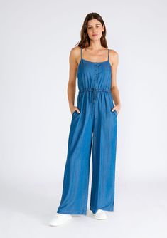 [Color: Vintage Wash] A front facing image of a brunette model wearing a classic denim blue sleeveless jumpsuit crafted from Tencel. With adjustable spaghetti straps Sleeveless Solid Denim Jumpsuit For Summer, Solid Sleeveless Denim Jumpsuit For Summer, Casual Sleeveless Solid Denim Jumpsuit, Casual Sleeveless Jumpsuit With Tie Waist, Spring Medium Wash Jumpsuits And Rompers With Adjustable Straps, Spring Denim Jumpsuits And Rompers With Adjustable Straps, Casual Sleeveless Overalls With Tie Straps, Bohemian Jumpsuit, Denim Jumper