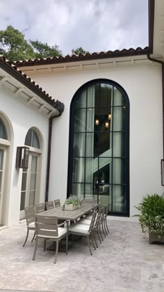 an outdoor dining table and chairs in front of a white stucco building with arched windows