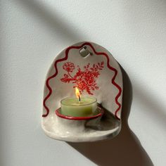 a small candle is lit in a ceramic dish with red trim on the edge and white wall behind it