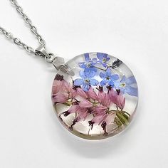 blue and pink flowers are in a glass dome on a silver chain, sitting on a white surface