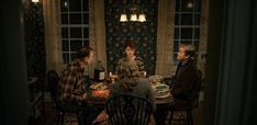 three people sitting at a table with food and wine in front of them on the dining room floor