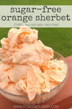 a glass bowl filled with orange ice cream on top of a wooden table next to grass