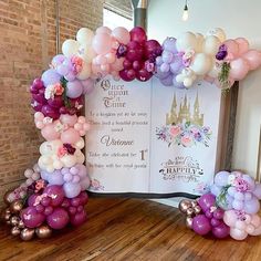 an arch made out of balloons and flowers on a wooden floor in front of a sign