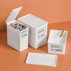 two white containers with toothbrushes in them on a brown surface next to another container