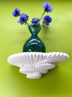 a green vase with three blue flowers in it on a table next to a white plate