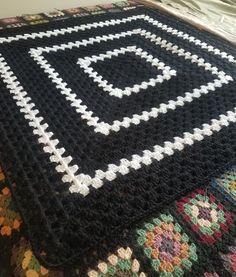 a crocheted blanket on top of a bed with a black and white design