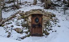 an old door in the middle of a snowy forest with rocks and trees around it