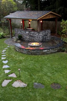 a backyard with a fire pit surrounded by grass and stone steps leading up to a shed