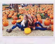 two women sitting on the ground surrounded by pumpkins