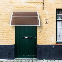 a green door and window in front of a yellow brick building with two windows on each side