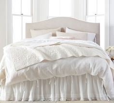 a white bed with ruffled bedspread and pillows