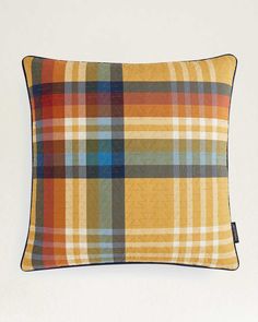 an orange and blue plaid pillow on a white wall