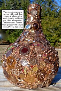 a vase with many buttons on it sitting on a wooden table in front of some trees