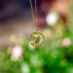 "A crescent moon pendant holds a tiny fern frond in this gold plated necklace. Jewelry grade resin encases the fern in the center of the pendant for a magical forest moon piece. Matching chain can be 18\" or 24\"- choose at checkout. Comes on a labeled card." Nature-inspired Moon Charm Pendant Necklace, Nature-inspired Necklace With Moon Charm Round Pendant, Nature-inspired Necklace With Round Moon Charm Pendant, Nature-inspired Round Pendant Necklace With Moon Charm, Nature-inspired Round Pendant Jewelry With Moon Charm, Nature-inspired Moon Charm Necklace As A Gift, Green Moon Charm Necklace, Nature-inspired Moon Charm Necklace As Gift, Nature-inspired Moon Charm Necklace For Gift