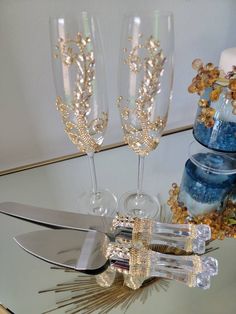 two champagne flutes with crystal stems on a glass table next to other decorations and cake