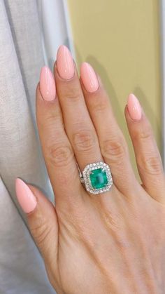 a woman's hand with pink manicured nails holding an emerald and diamond ring