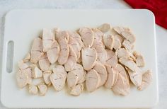 sliced chicken on a white cutting board next to a red napkin and knife, ready to be cooked