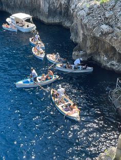 several small boats are in the water near some rocks and cliffs, with people on them