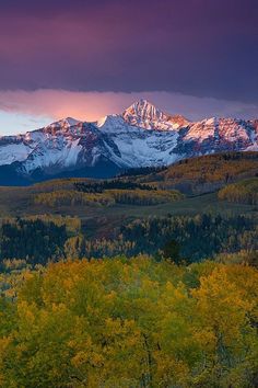 the mountains are covered in snow and trees with yellow leaves on them as the sun sets