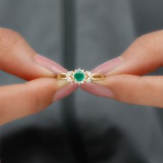 a woman's hand holding an emerald and diamond ring