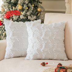 two white pillows sitting on top of a couch next to a christmas tree