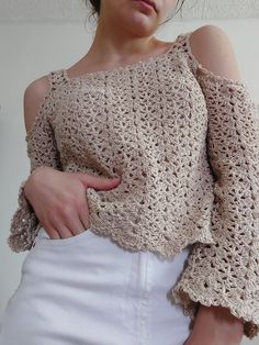 a woman is wearing a crocheted top and white skirt with her hands on her hips