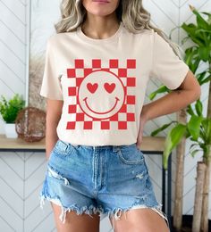 Retro Checkered Smiley Face With Heart Eyes 😍 Shirt Or Sweatshirt Printed on Unisex Bella and Canvas shirts or Unisex Gildan Crewneck Sweatshirts. Please refer to the size charts to find the right fit for your style 💖. Although Unisex, most women feel they fit pretty true to size.   DESIGN/PRINTING: We use DTG (Direct To Garment) Printing which ensures the highest quality of details, color, and durability. MATERIALS: .: Solid Bella and Canvas colors are 100% Soft Cotton .: Heather colors and S Casual Heart Print T-shirt For Spring, Casual Heart Print T-shirt With Relaxed Fit, Retro Cotton T-shirt With Heart Graphic, Casual Short Sleeve Tops With Heart Graphic, Spring Heart Print Crew Neck Tops, Summer Long Sleeve Tops With Heart Graphic, Long Sleeve Summer Tops With Heart Graphic, Trendy Crew Neck Top With Heart Graphic, Trendy Cotton T-shirt With Heart Print