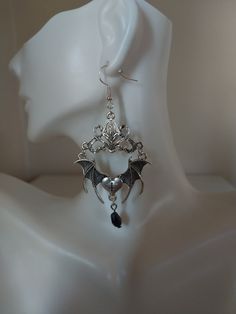 Unveil your daring side with our spellbinding Gothic Bat Earrings. Crafted in the captivating Tibetan silver style, these unique earrings feature intricately designed bats and a raised connector, all adorned with a mesmerizing black teardrop crystal. Embrace the allure of the night with our exquisitely detailed bat-shaped earrings, symbolizing mystery and transformation for those who appreciate the enigmatic. Each pair of Gothic Bat Earrings is meticulously handcrafted with skill and passion, ensuring a high level of artistry and quality. Their darkly stylish and bold design allows them to seamlessly complement various outfits, from casual wear to formal attire. For those seeking an accessory that stands out from the crowd, our Gothic Bat Earrings are the perfect choice to draw attention a Silver Winged Fantasy Jewelry, Elegant Winged Metal Jewelry, Gothic Dangle Metal Plug Earrings, Gothic Metal Dangle Plug Earrings, Fantasy Dangle Earrings For Halloween, Gothic Metal Plug Earrings With Ear Wire, Halloween Fantasy Earrings For Pierced Ears, Fantasy Halloween Earrings For Pierced Ears, Halloween Fantasy Dangle Earrings