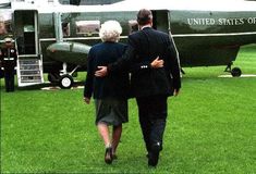 two people walking towards an air force plane on the grass with another person in suit and tie