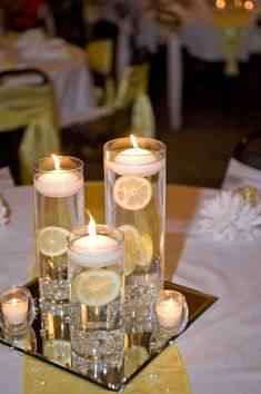 candles are lit in glass vases with lemon slices on the center table at a wedding reception