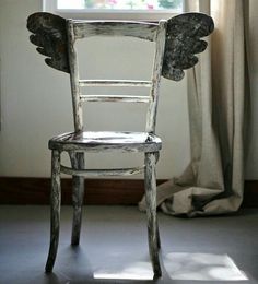 an old wooden chair sitting in front of a window with angel wings on it's back