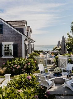 there is a patio with lawn chairs and tables in front of the house by the water