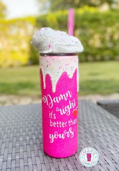 a pink cup with white frosting and sprinkles sitting on top of a table