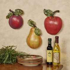 three apples and two pears hanging on a wall next to plates, wine bottles and plants