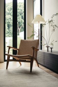 a wooden chair sitting in front of a window next to a lamp and planter