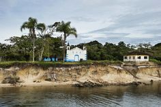 a white house sitting on top of a cliff next to the ocean with palm trees