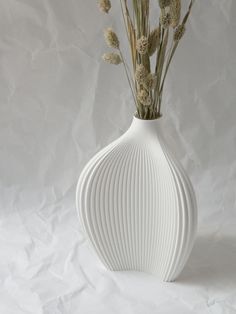 a white vase filled with flowers on top of a white tablecloth covered floor next to a wall