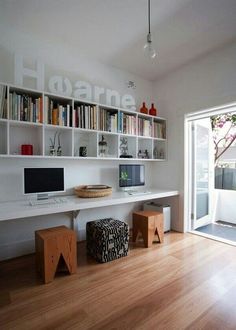 there is a desk with two computers on it and bookshelves above the desk